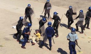 Riot police surround a protester during a rally against the introduction of bond notes by Zimbabwe’s central bank. / Photo Credit: Tsvangirayi Mukwazhi/AP